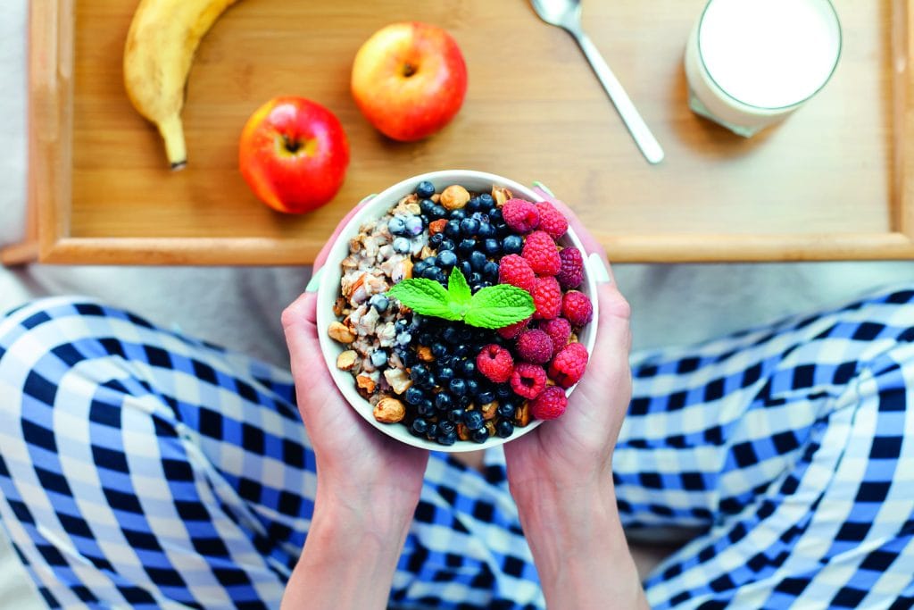 Females hands hold a bowl of granola with fresh with fresh raspberries and blueberries. Healthy breakfast in the morning. ?lose-up. Top view. Females hands hold a bowl of granola with fresh with fresh raspberries and blueberries. Healthy breakfast in the morning. ?lose-up. Top view.