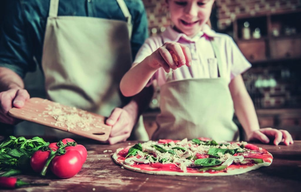 Dad and daughter cooking Cute little girl and her handsome dad in aprons are smiling while cooking pizza in kitchen