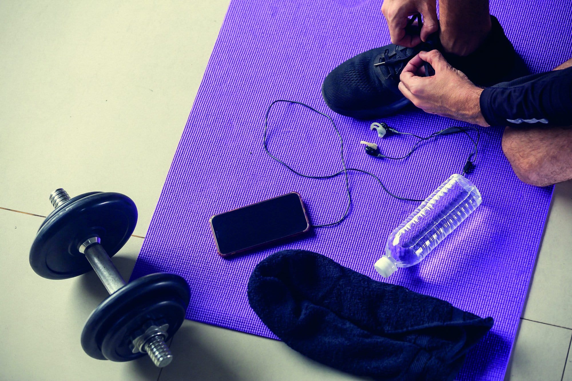 Young man tying shoelaces on floor. Ready for gym workout. Healthy lifestyle, sport or athlete's equipment on bright mat background. Flat lay. Top view
