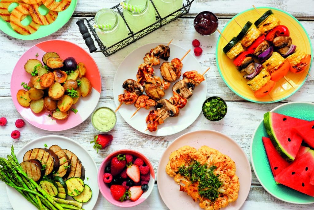 Vegan summer bbq or picnic table scene on a white wood background Vegan summer bbq or picnic table scene. Overhead view on a white wood background. Fruit, grilled vegetables, skewers, cauliflower steak and lemonade. Meat substitute concept.