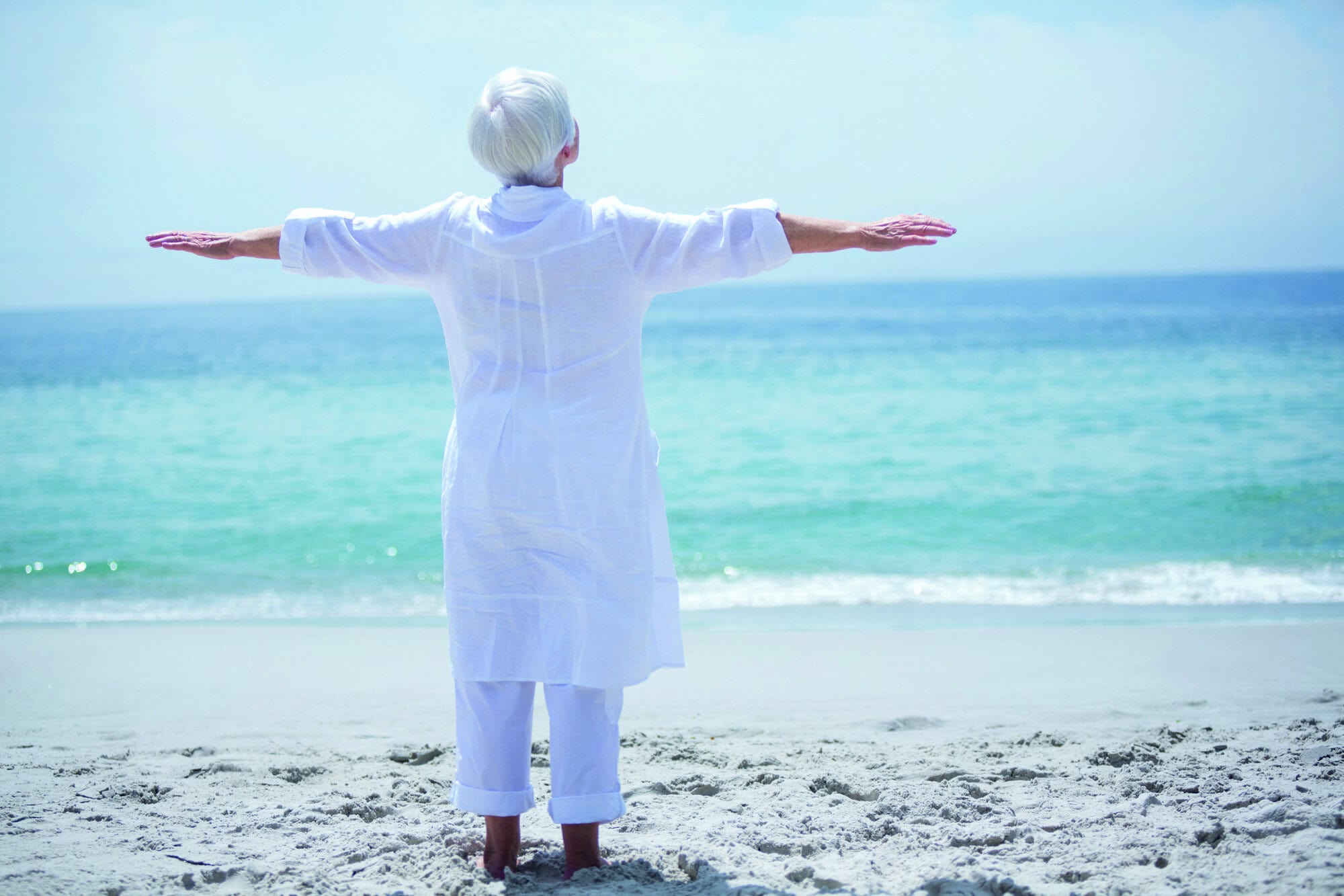 Rear view of senior woman exercising at sea shore on sunny day