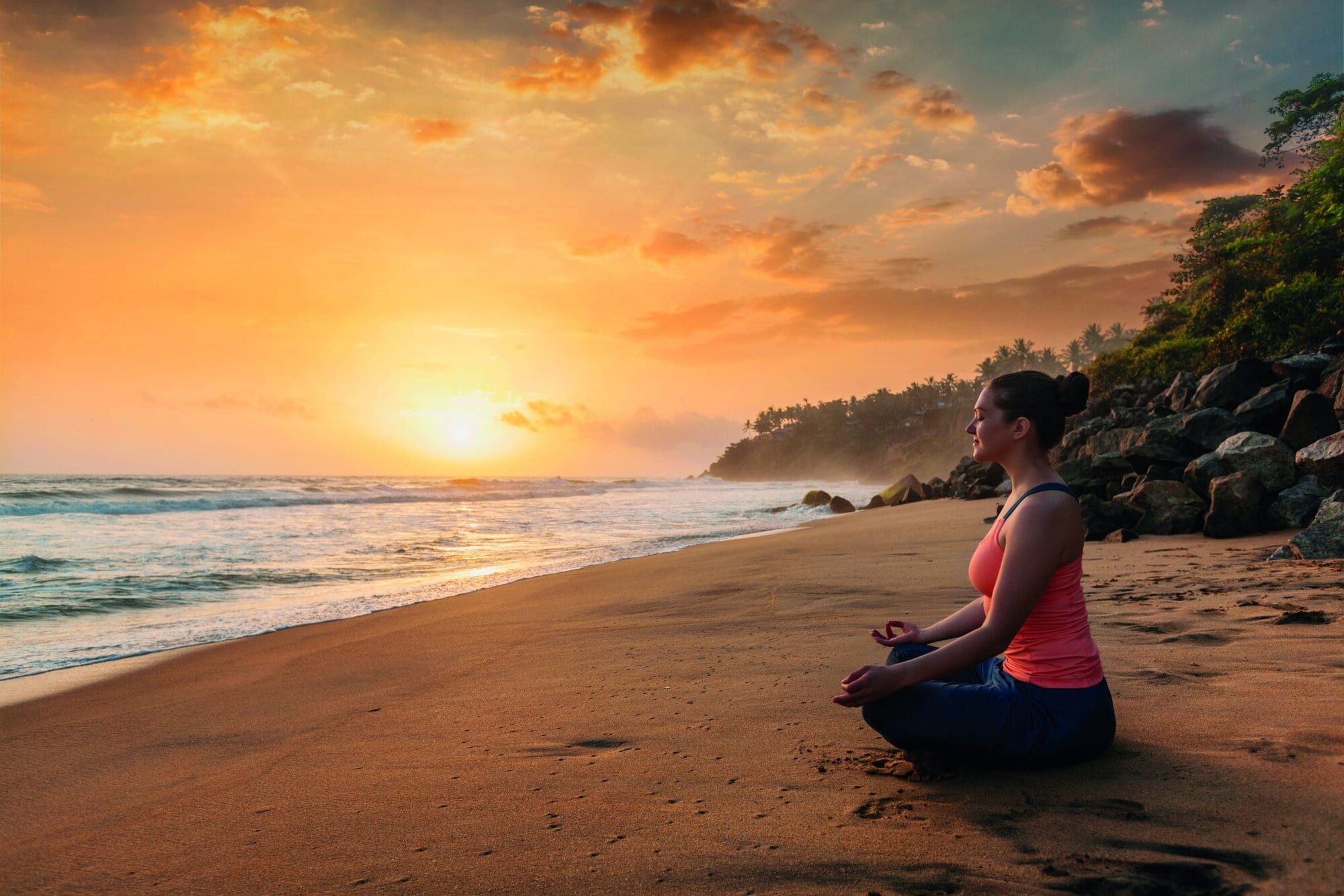 Woman doing yoga - meditate and relax in Padmasana Lotus asana pose with chin mudra outdoors at tropical beach on sunset with dramatic sun