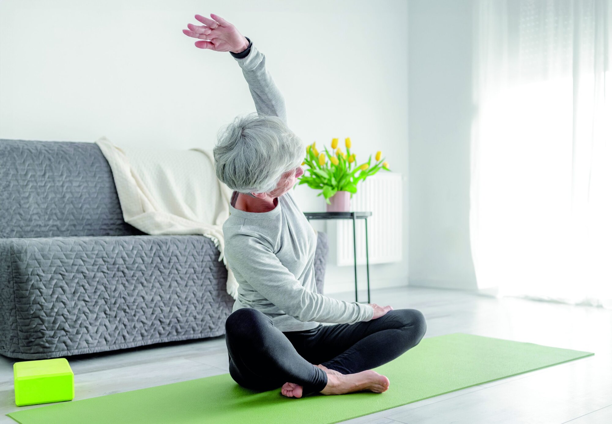Calm Home Exercises In A Bright Room, A 70-Year-Old Woman Practices Yoga