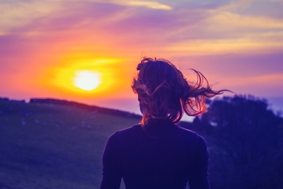 Young woman admiring the sunset over fields