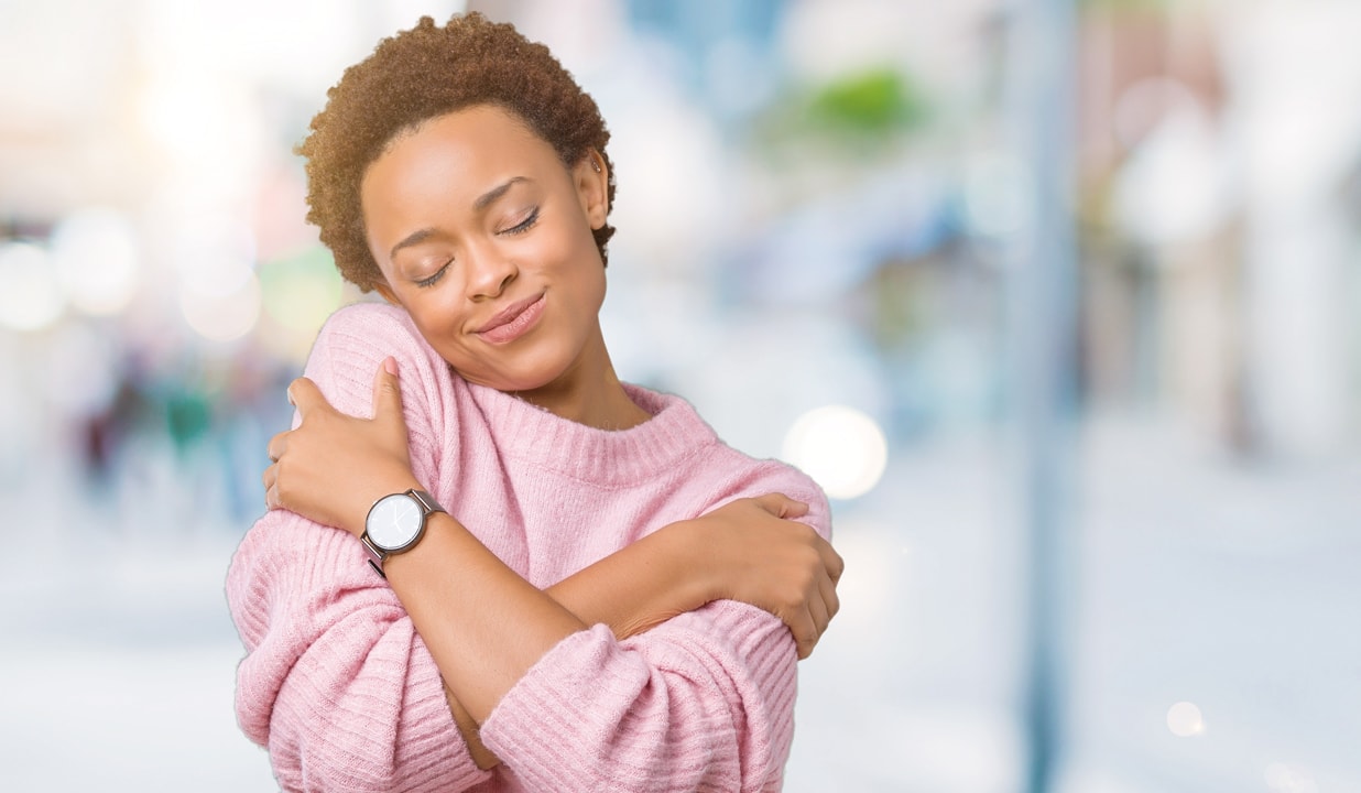 Beautiful young african american woman over isolated background Hugging oneself happy and positive, smiling confident. Self love and self care