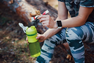 Sporty Woman Eating Protein Bar and drinking an amino acid cocktail. Woman in military-colored clothing in forest