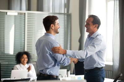 Smiling middle-aged ceo promoting motivating worker shaking hands congratulating with achievement promising respect bonus thanking for good work, team applauding, employee reward recognition concept