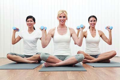 An interracial group of three beautiful young women sitting cross legged in a yoga or pilates position at a gym and weight training