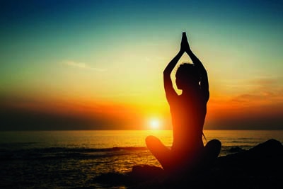Yoga woman silhouette. Meditation on the ocean during amazing sunset.