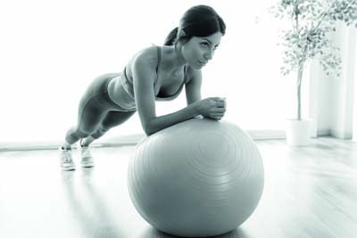 Portrait of beautiful young woman doing pilate exercise with fitness ball at home.