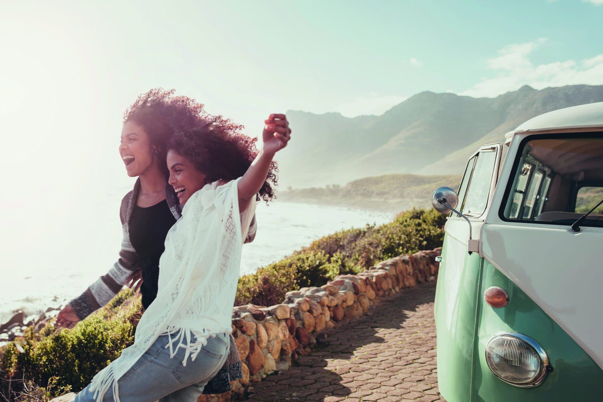 Female friends on road trip enjoying outdoors on a sunny day. Women standing outside van  and laughing.