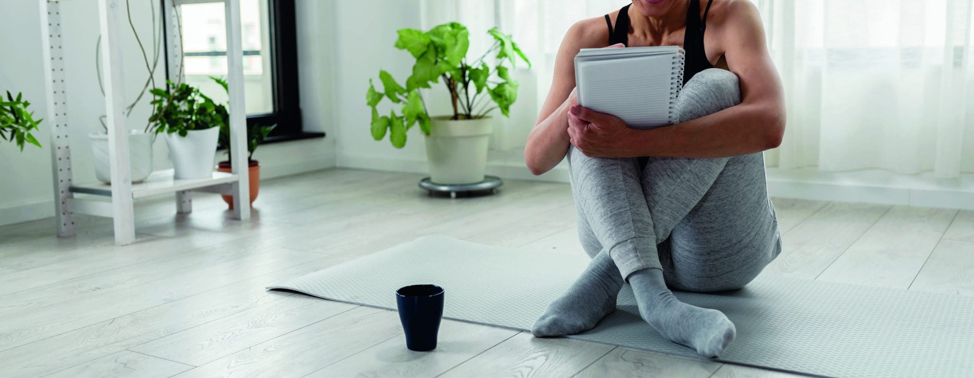 Young woman writing in her notebook. Sitting at home by the window on a yoga mat after exercise. Personal growth resolutions