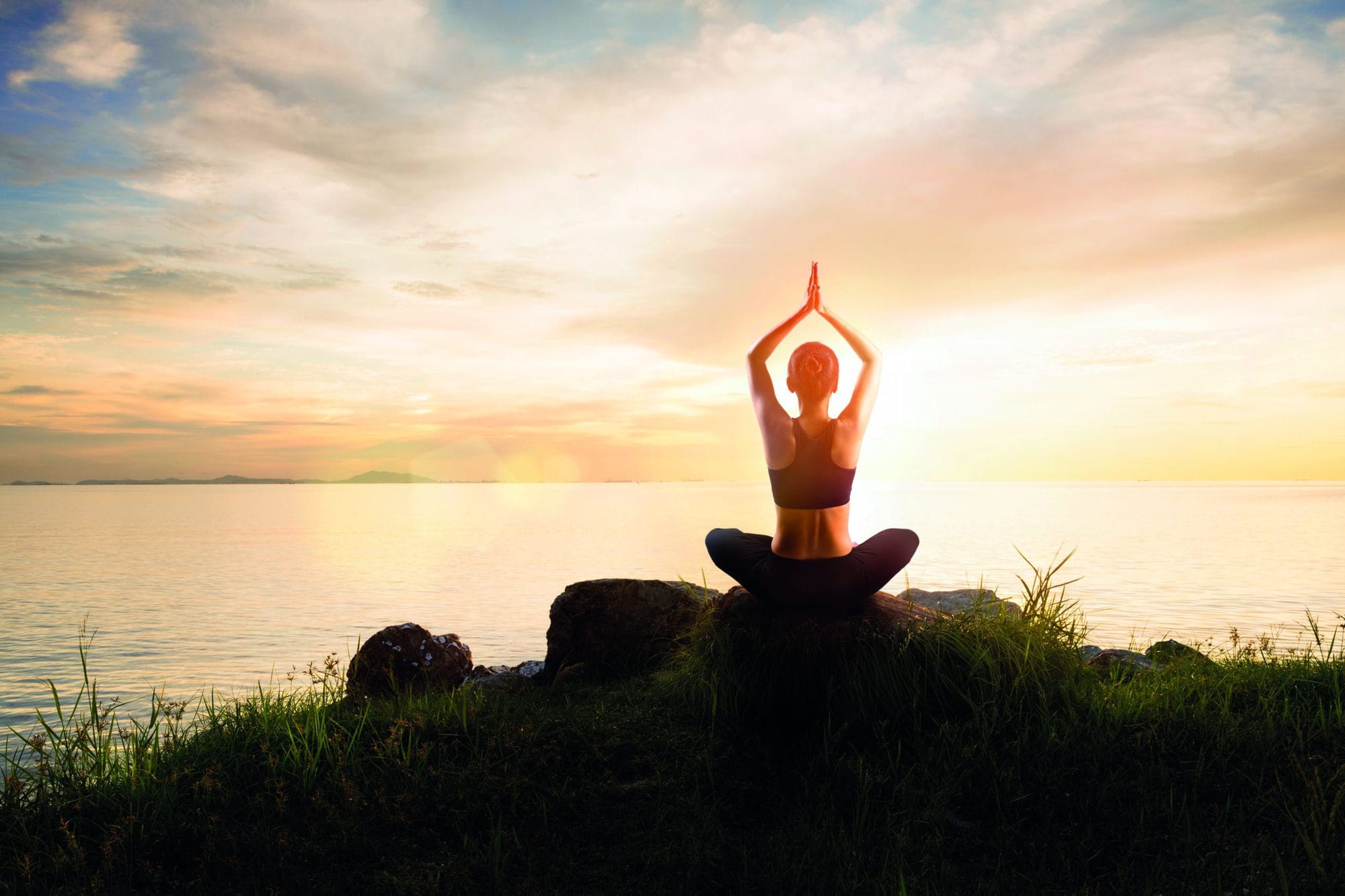 Woman meditating in a yoga pose on the beach at sunset, Yoga is a physical, spiritual practice or discipline, Yoga which originated in India