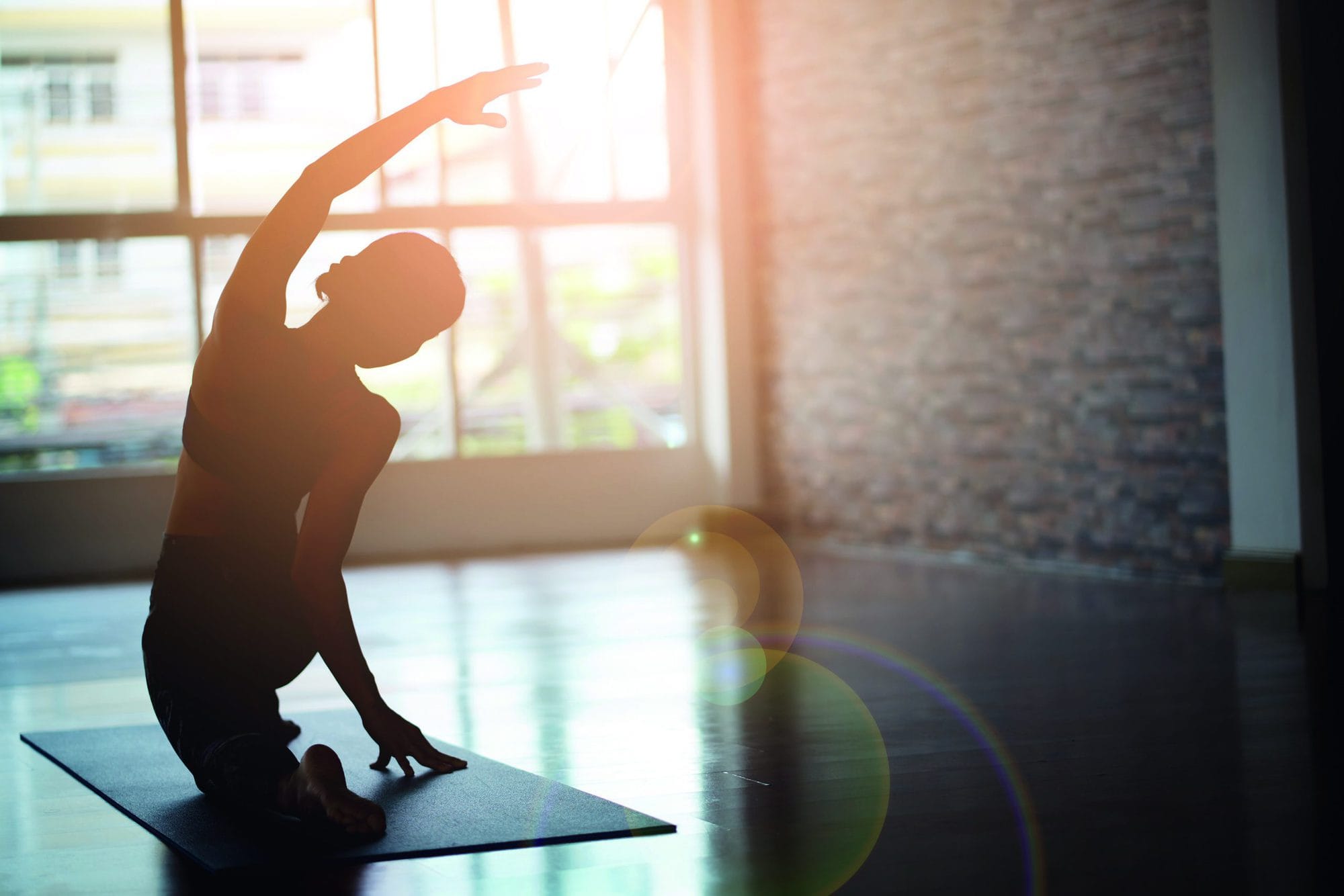 Asian woman doing yoga in a room with sunlight coming through the window.