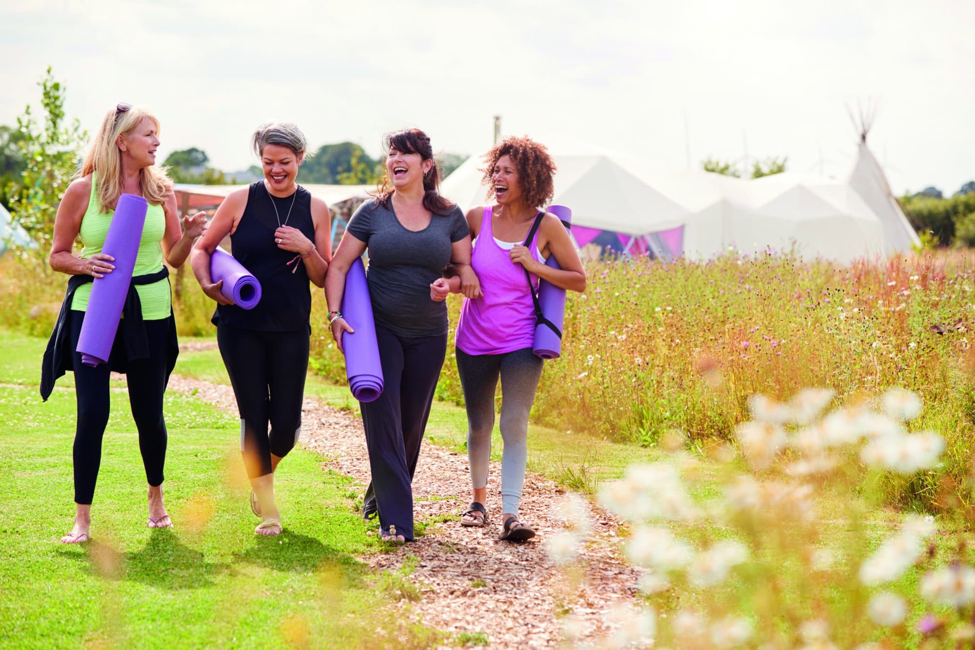 Group Of Mature Female Friends On Outdoor Yoga Retreat Walking Along Path Through Campsite