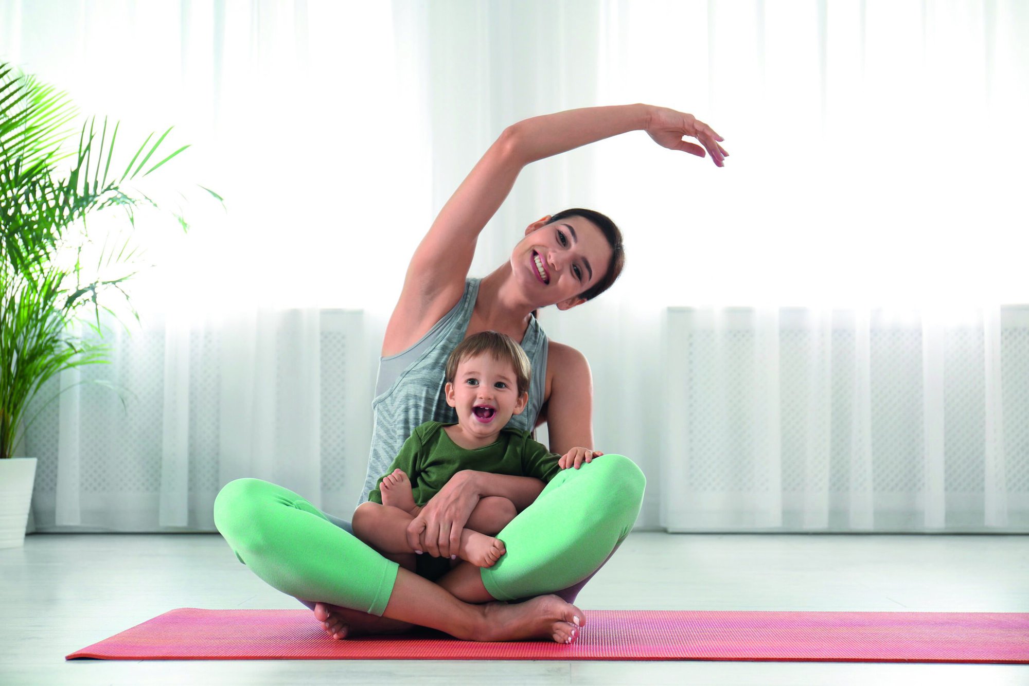 Young woman doing exercise with her son indoors. Home fitness