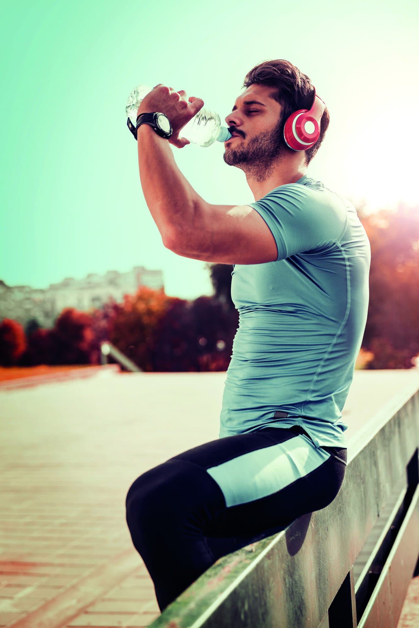 Portrait of young man drinking some water from a bottle while sitting and resting after training.