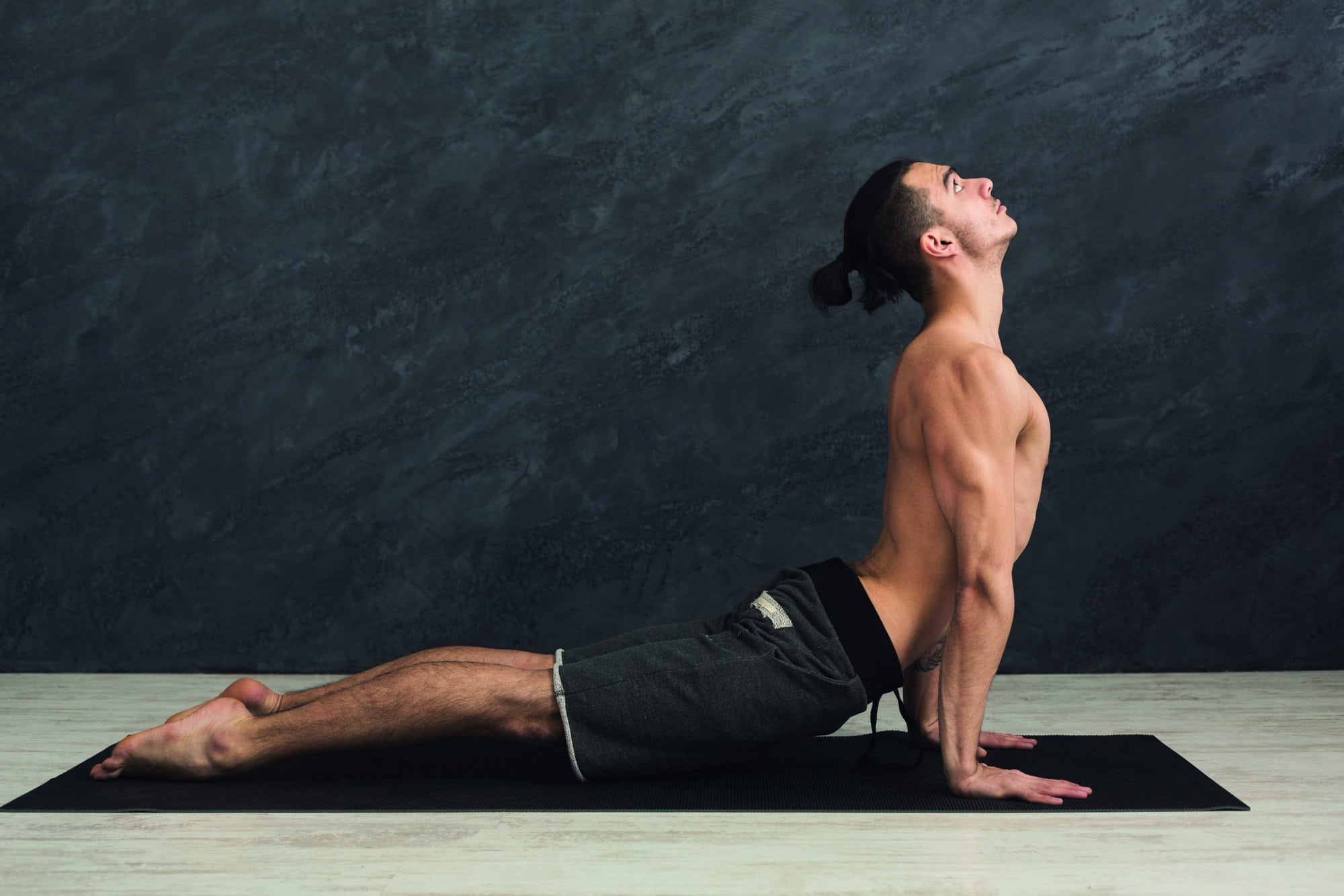 Man doing yoga. Sportsman doing Cobra posture, stretching back on mat at gray background, copy space