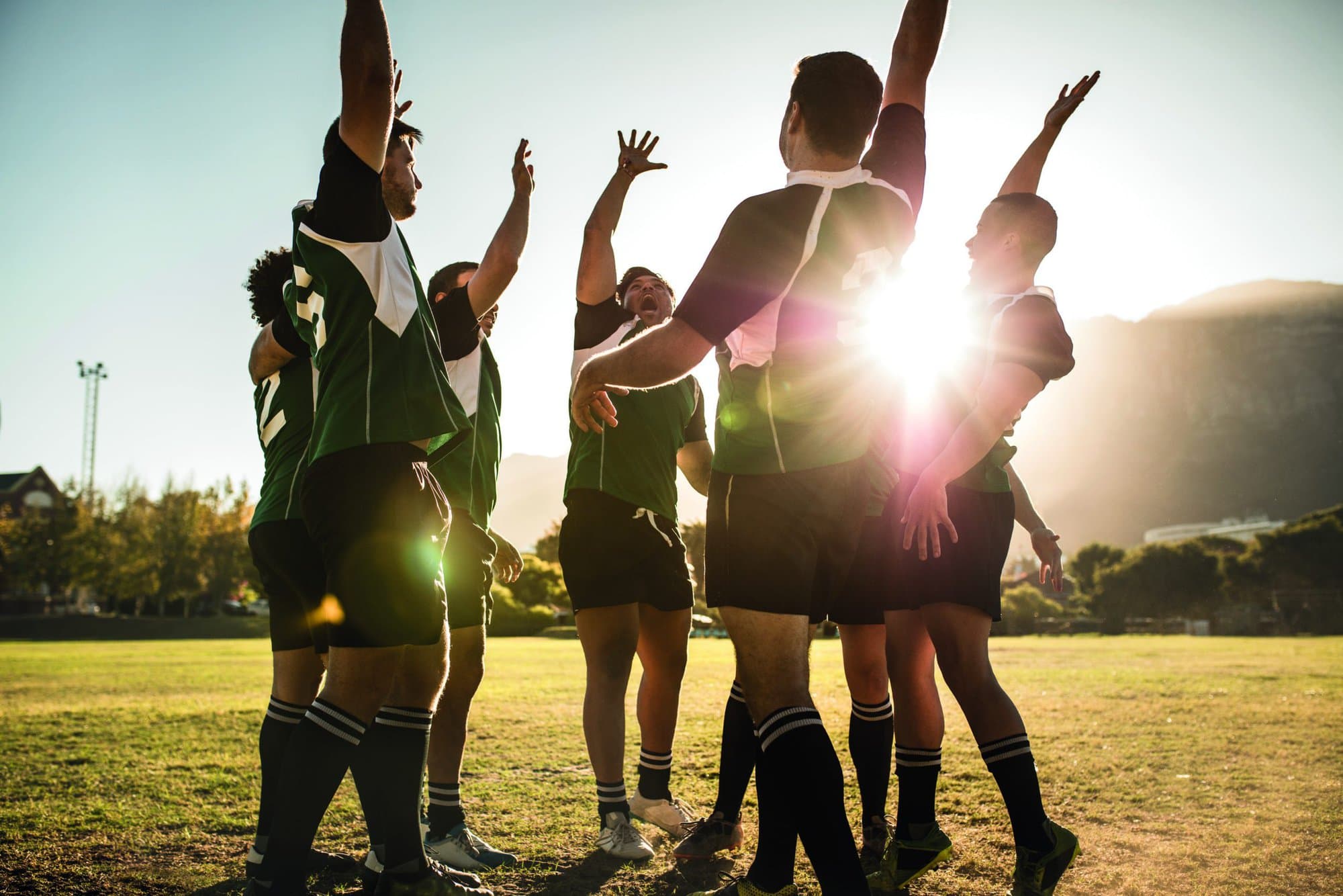 Rugby players celebrating a win at the sports field. Rugby team with hands raised and screaming after victory.