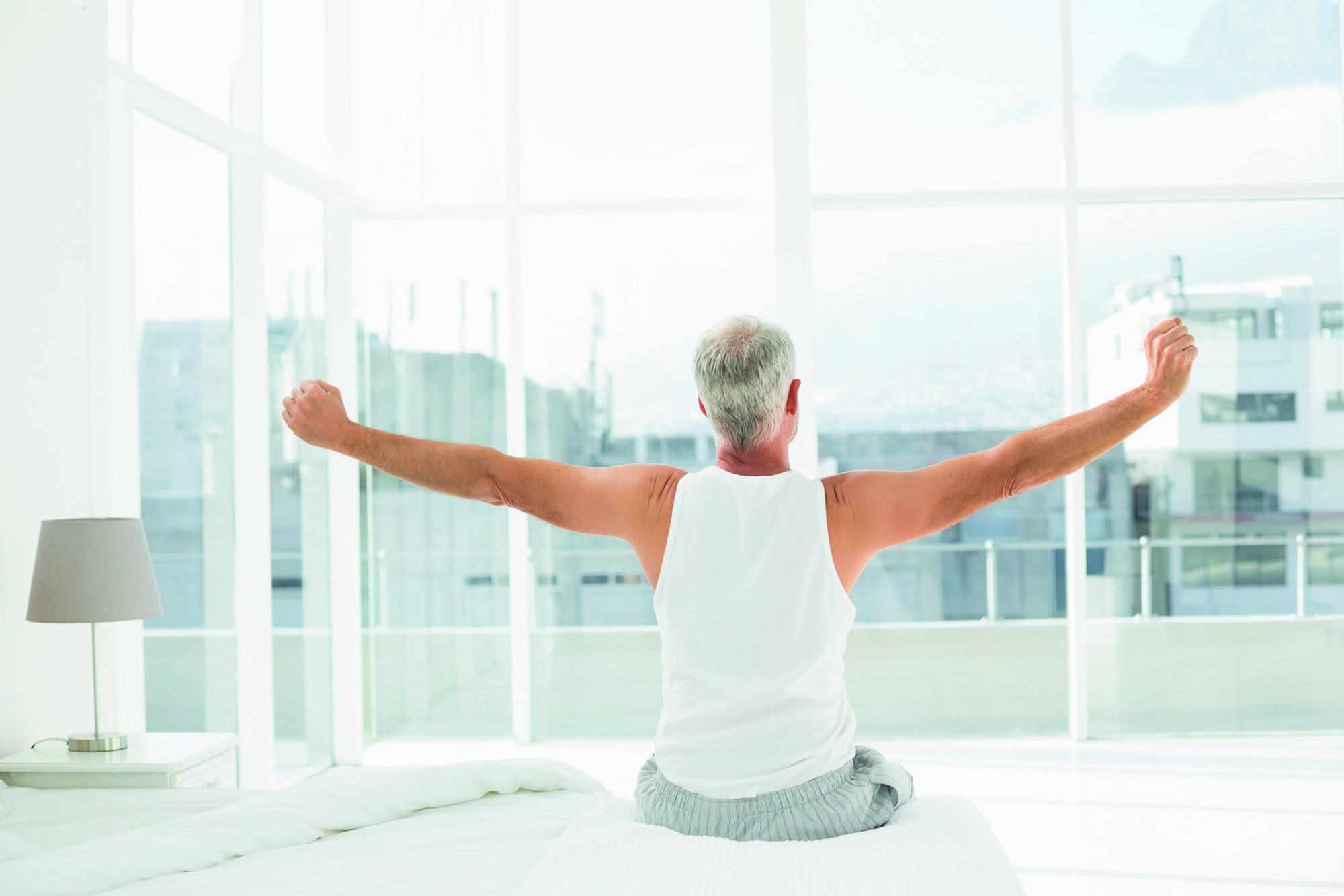 Rear view of a mature man waking up in bed and stretching his arms