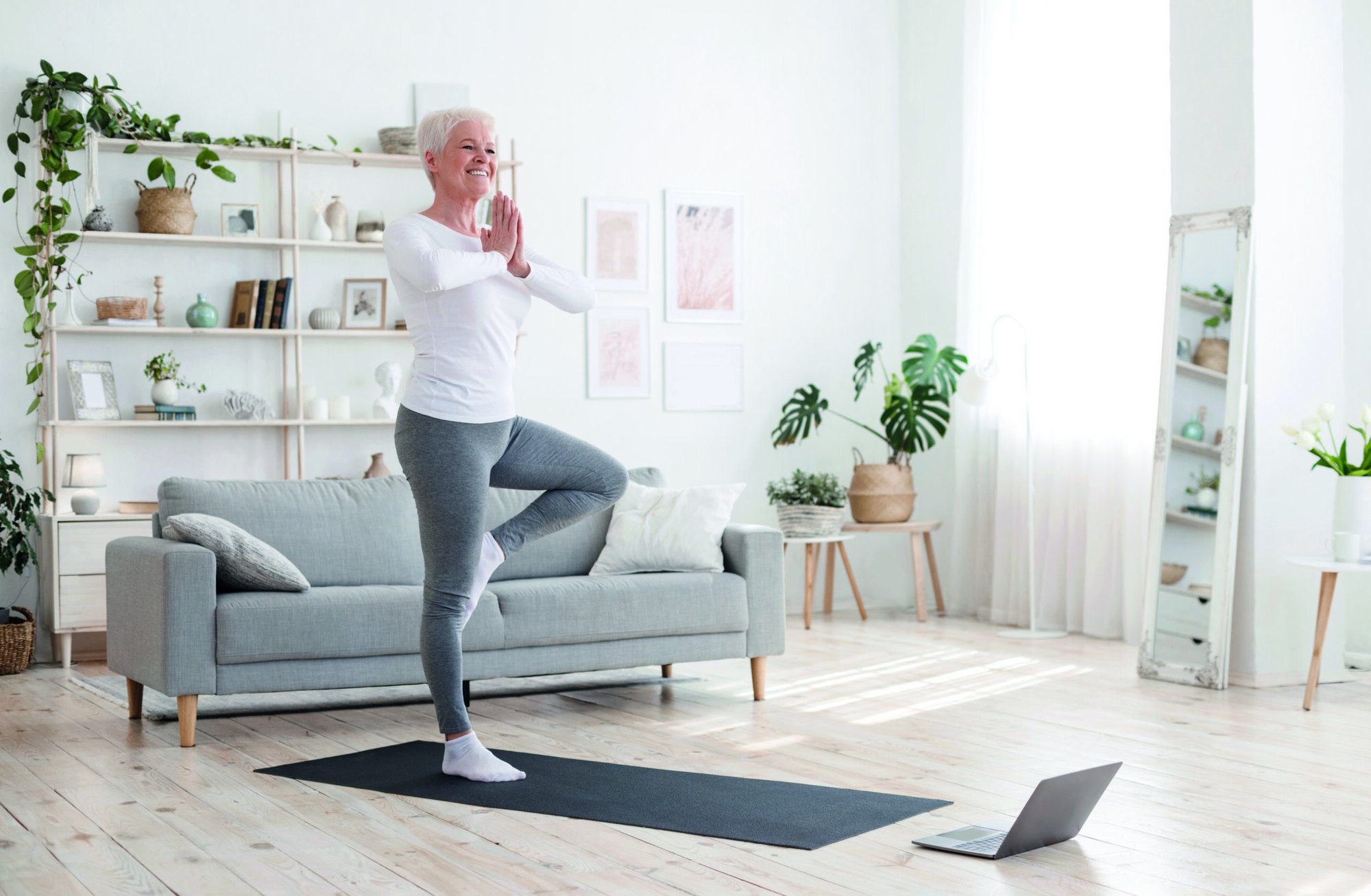 Sporty,Senior,Woman,Practicing,Yoga,With,Online,Tutorials,At,Home, Sporty Senior Woman Practicing Yoga With Online Tutorials At Home, Standing In Tree Pose And Smiling, Enjoying Retirement Time, Free Space