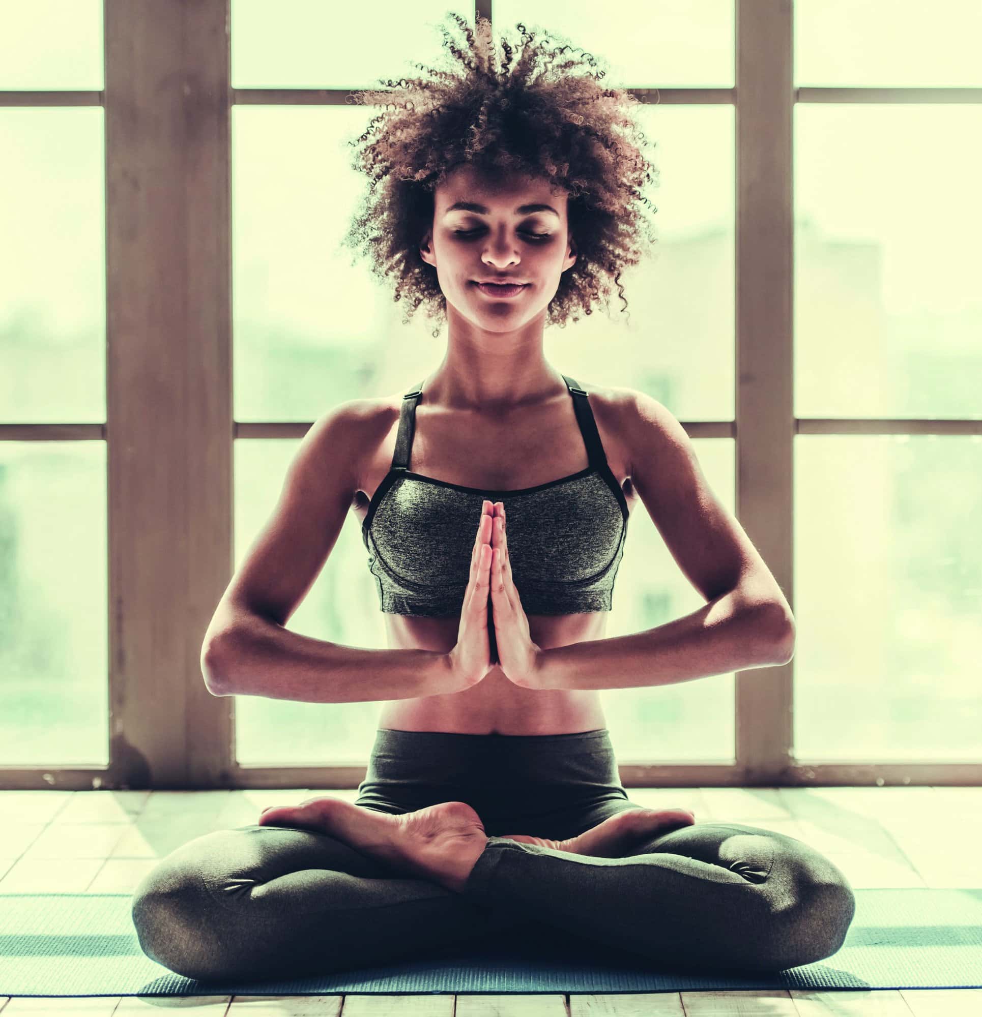 Attractive Afro American girl in sportswear is doing yoga and smiling