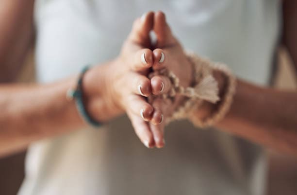 Cropped shot of an unrecognizable woman standing with her palms together while meditating indoors