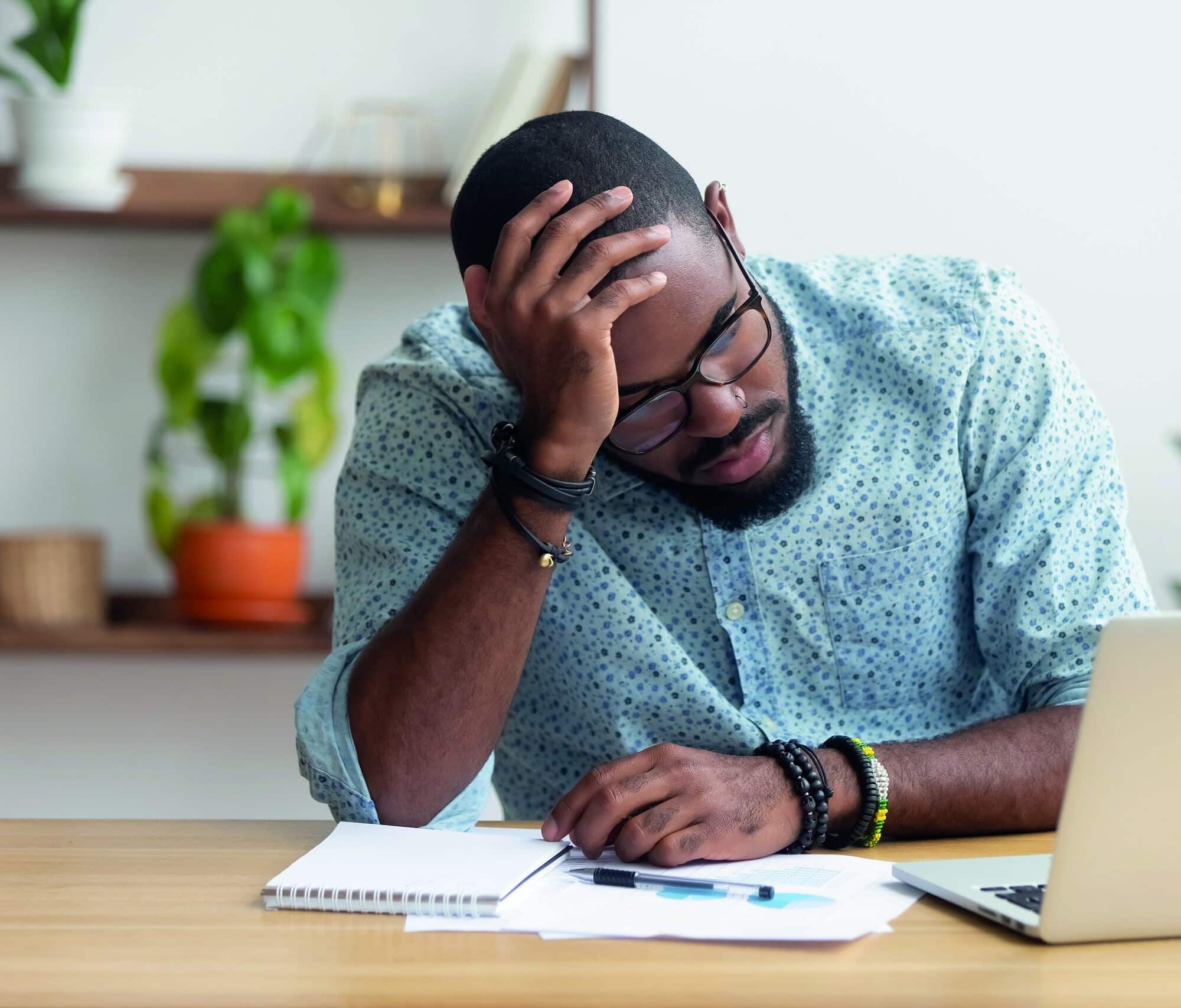 Tired depressed bored african businessman frustrated by business failure bankruptcy looking at laptop feel exhausted having headache, upset stressed black office worker worried about problem at work