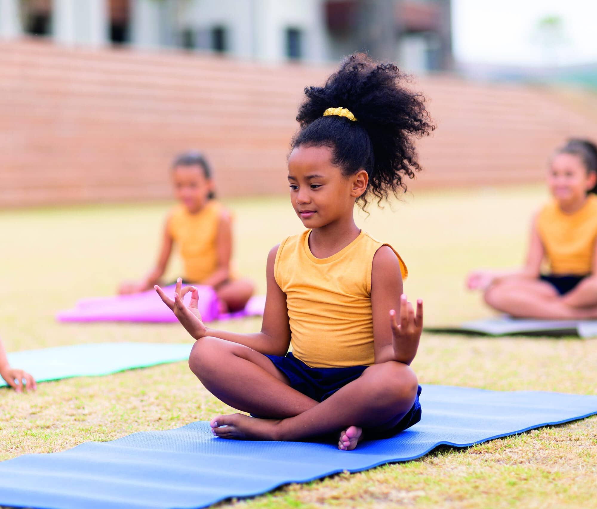 Multiracial elementary schoolgirls with gesturing while sitting on yoga mat at school ground. unaltered, childhood, education, activity, sports training, yoga and physical education concept.