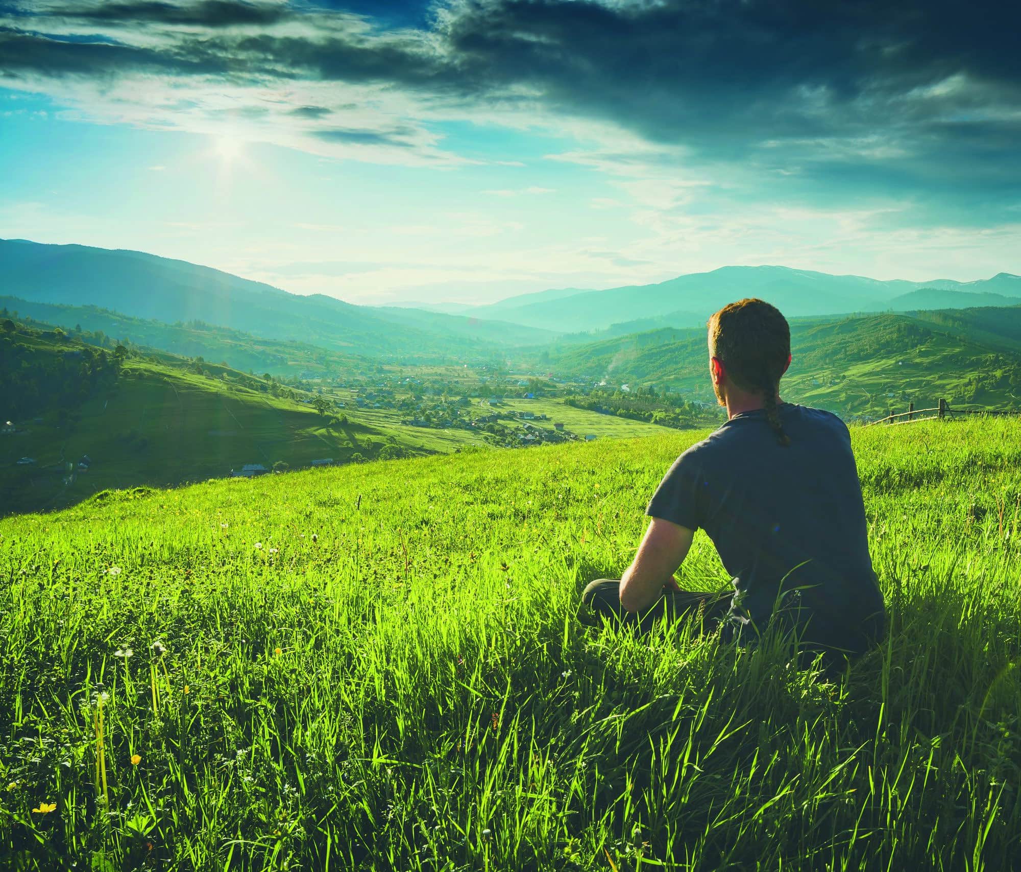 Tourist sitting on a hill in a green grass and enjoy majestic sunset above carpathian mountain valley. Instagram stylization.