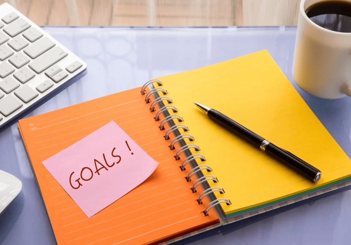 Goals setting for year resolution and new project Goals word on note pad stick on blank colorful paper notebook at workspace, year resolution concepts