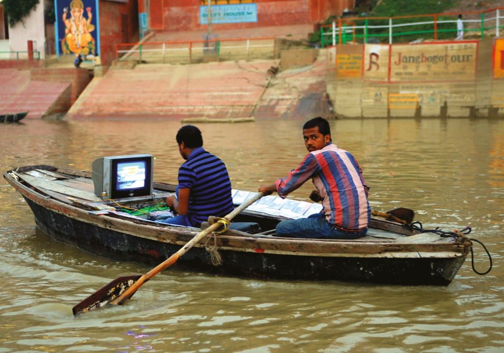 Two men in boat watching television.