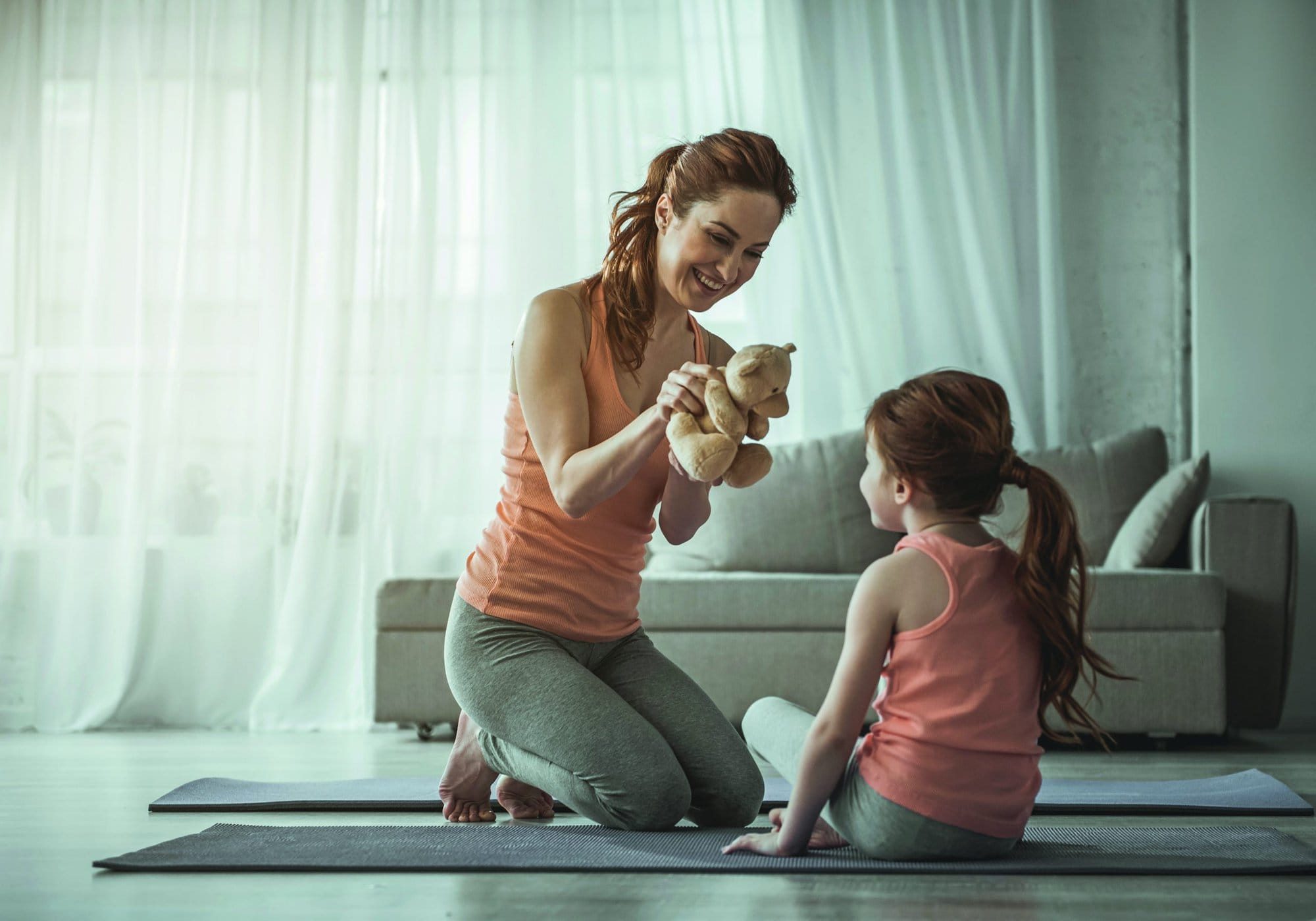 Fun time. Full length portrait of woman and child sitting on floor. Mom is holding teddy bear in her hands and jocosely smiling. Copy space in left side