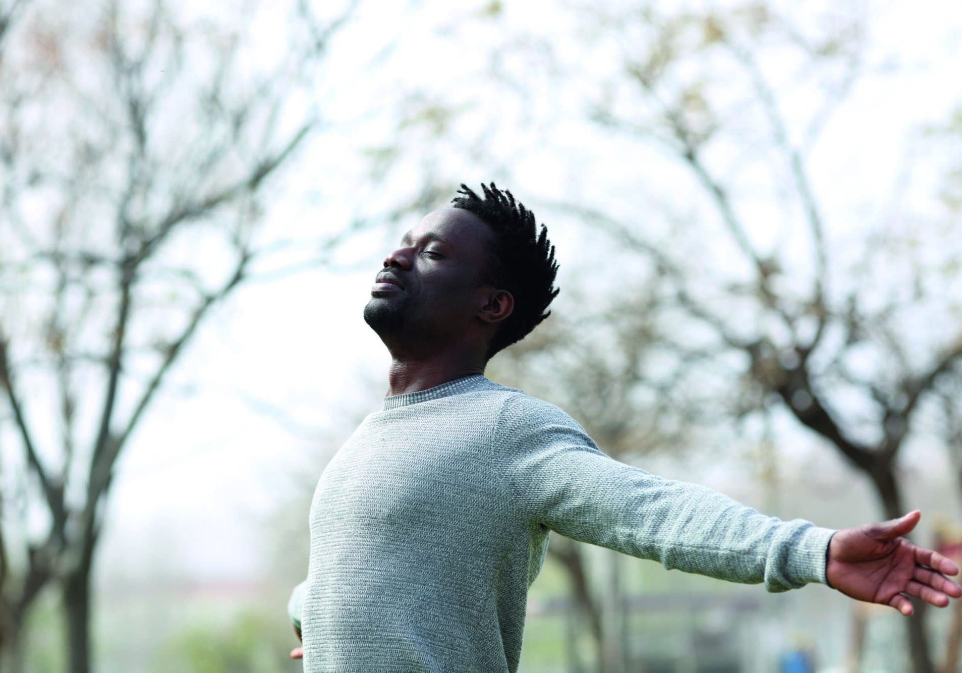 Satisfied black man breathing fresh air with eyes closed standing in the park outdoors