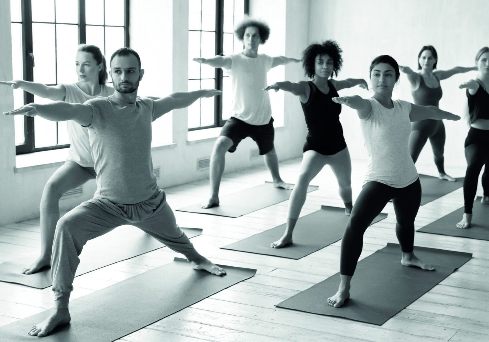 Focused sporty handsome young male trainer leading yoga class for concentrated multiracial students, practicing virabhadrasana second warrior II position together at yoga training in modern studio.