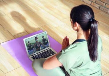 Young woman meditating watching live online tv pilates group class tutorial on laptop computer at home doing yoga virtual training fitness workout meditation exercise stream. Over shoulder screen view